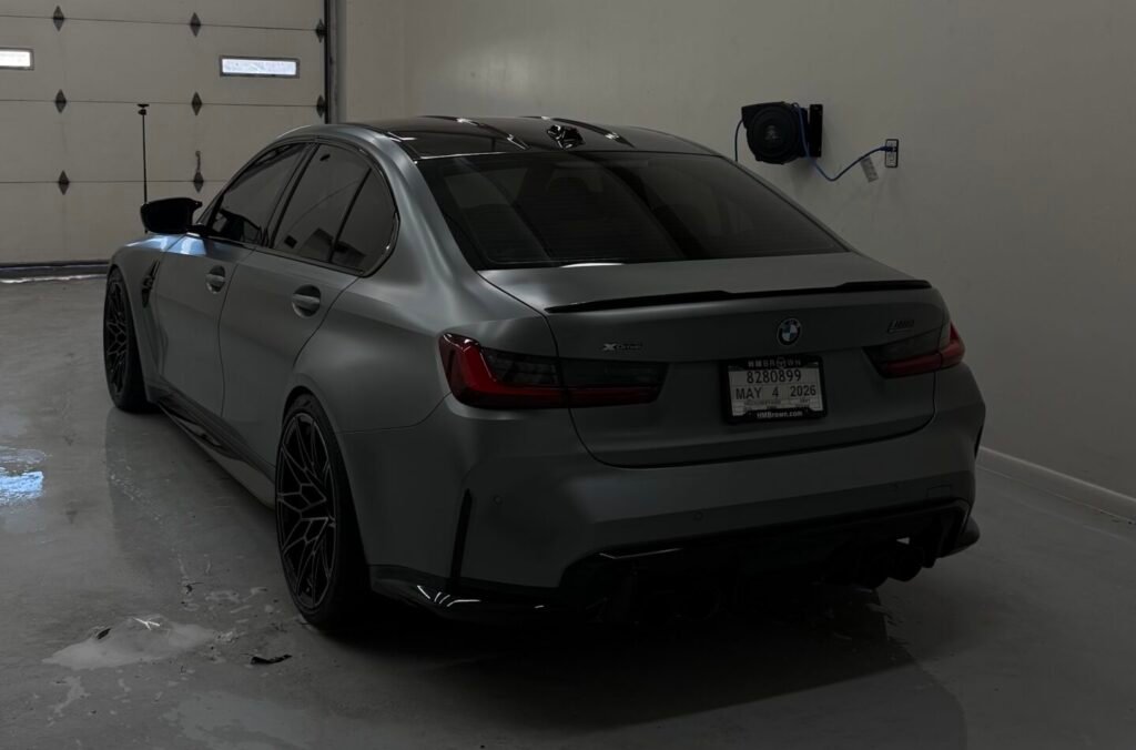 Matte gray BMW sedan inside professional auto detailing studio with clean polished floor and overhead lighting